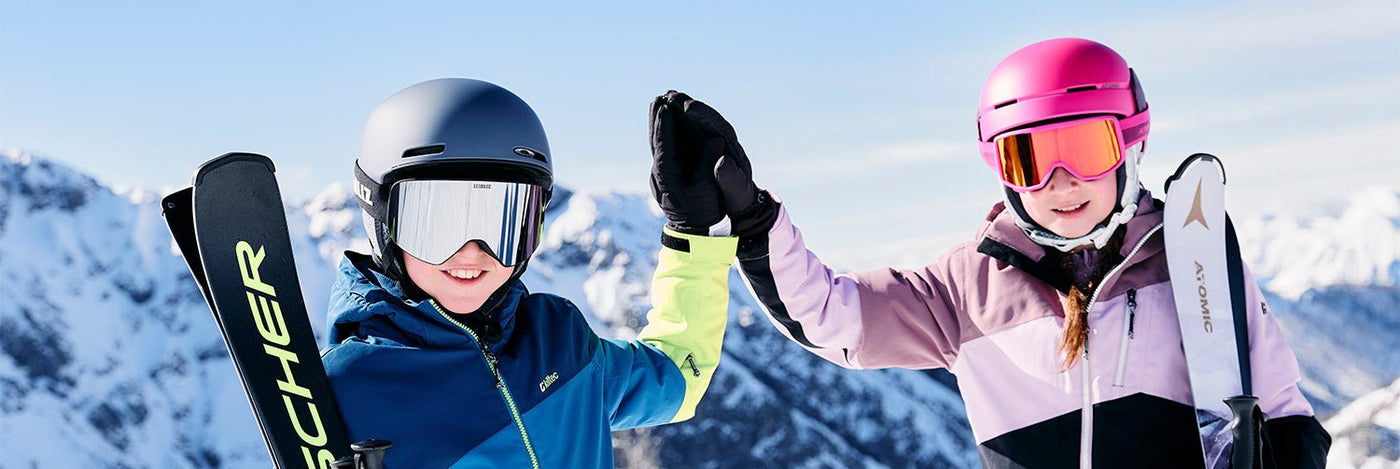 Kinder beim Apin Skifahren im Hintergrund eine schneebedeckte Berglandschaft
