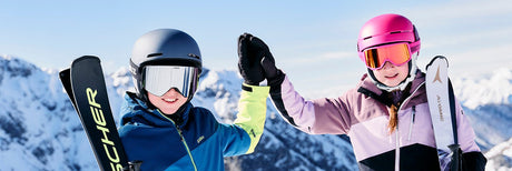 Kinder beim Apin Skifahren im Hintergrund eine schneebedeckte Berglandschaft