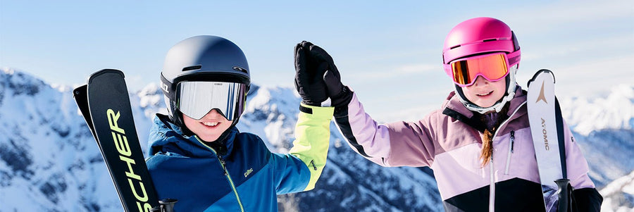 Kinder beim Apin Skifahren im Hintergrund eine schneebedeckte Berglandschaft